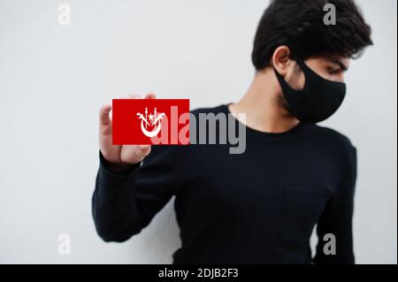 Malaiischer Mann tragen ganz schwarz mit Gesichtsmaske halten Kelantan Flagge in der Hand isoliert auf weißem Hintergrund. Staaten und Bundesgebiete von Malaysia coronaviru Stockfoto