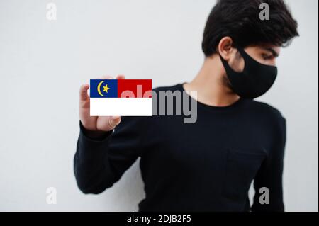 Malaiischer Mann tragen ganz schwarz mit Gesichtsmaske halten Malacca Flagge in der Hand isoliert auf weißem Hintergrund. Staaten und Bundesgebiete von Malaysia Coronavirus Stockfoto