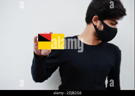 Malaiischer Mann tragen ganz schwarz mit Gesichtsmaske halten Negeri Sembilan Flagge in der Hand isoliert auf weißem Hintergrund. Staaten und Bundesgebiete von Malaysia cor Stockfoto