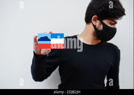 Malaiischer Mann tragen ganz schwarz mit Gesichtsmaske halten Sabah Flagge in der Hand isoliert auf weißem Hintergrund. Staaten und Bundesgebiete von Malaysia Coronavirus c Stockfoto