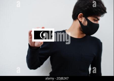 Malaiischer Mann tragen ganz schwarz mit Gesichtsmaske halten Terengganu Flagge in der Hand isoliert auf weißem Hintergrund. Staaten und Bundesgebiete von Malaysia coronavi Stockfoto