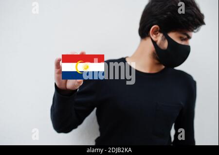 Malaiischer Mann tragen ganz schwarz mit Gesichtsmaske halten Labuan Flagge in der Hand isoliert auf weißem Hintergrund. Staaten und Bundesgebiete von Malaysia Coronavirus Stockfoto