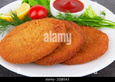 Fischpfannkuchen auf Teller mit Ketchup, auf dunkler Oberfläche Stockfoto
