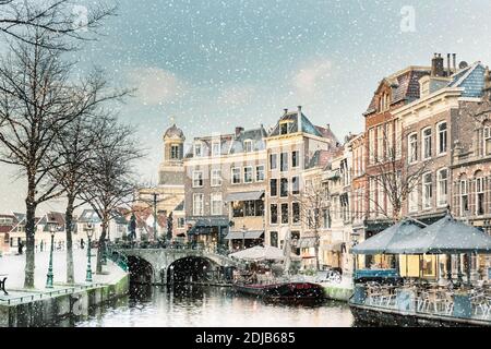 Winteransicht mit Schneefall des niederländischen Nieuwe Rijn-Kanals mit Brücke und historischen Gebäuden im Stadtzentrum von Leiden, Niederlande Stockfoto