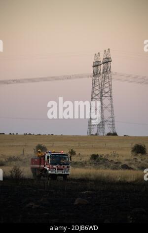 Melbourne, Australien 14 Dec 2020, EIN Feuerwehrauto der County Fire Authority fährt mit seiner Crew über die verbrannten Fahrerlager in der Nähe von Mount Cottrell mit den Hochspannungsleitungen im Hintergrund. Die Feuerwehr hat mit Flugzeugen und Feuerwehrmannschaften einen 110 Hektar großen Grasbrand im äußersten Westen Melbournes kontrolliert, der mehrere Schuppen und Autos zerstört. Stockfoto