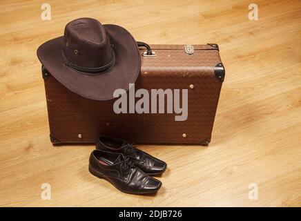 Set aus Herren Filzhut, schwarzen Schuhen und einem Koffer auf einem Holzboden Stockfoto