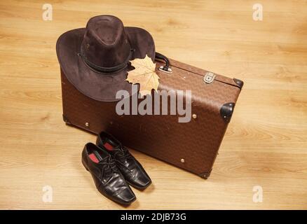 Set aus Herren Filzhut mit einem gelben Ahornblatt, schwarzen Schuhen und einem Koffer auf einem Holzboden Stockfoto