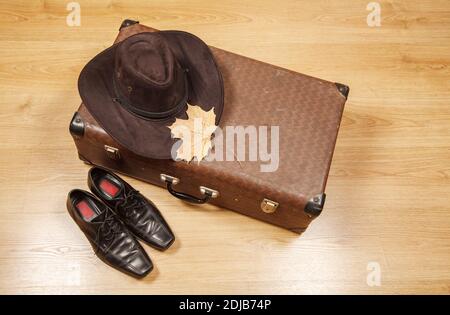 Set aus Herren Filzhut mit einem gelben Ahornblatt, schwarzen Schuhen und einem Koffer auf einem Holzboden Stockfoto