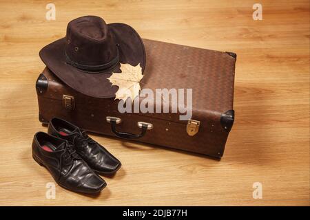 Set aus Herren Filzhut mit einem gelben Ahornblatt, schwarzen Schuhen und einem Koffer auf einem Holzboden Stockfoto