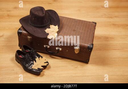 Set aus Herren Filzhut mit einem gelben Ahornblatt, schwarzen Schuhen und einem Koffer auf einem Holzboden Stockfoto