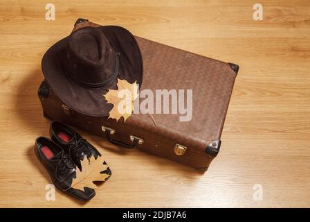 Set aus Herren Filzhut mit einem gelben Ahornblatt, schwarzen Schuhen und einem Koffer auf einem Holzboden Stockfoto