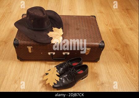 Set aus Herren Filzhut mit einem gelben Ahornblatt, schwarzen Schuhen und einem Koffer auf einem Holzboden Stockfoto