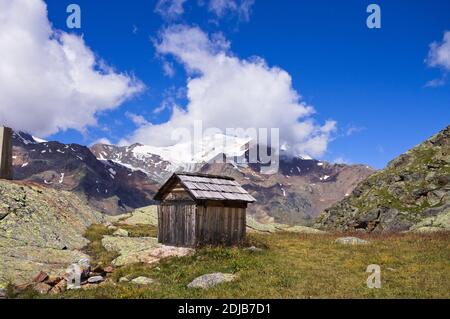 Ein isolierter Holzschuppen mit verschneiten Bergen im Hintergrund in den italienischen Alpen (Trentino, Italien, Europa) Stockfoto