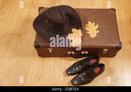 Set aus Herren Filzhut mit einem gelben Ahornblatt, schwarzen Schuhen und einem Koffer auf einem Holzboden Stockfoto