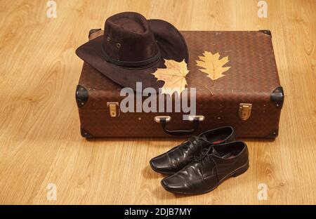 Set aus Herren Filzhut mit einem gelben Ahornblatt, schwarzen Schuhen und einem Koffer auf einem Holzboden Stockfoto