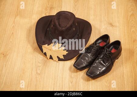 Set von Herren Filzhut mit einem gelben Ahornblatt Und schwarze Schuhe auf einem Holzboden Stockfoto