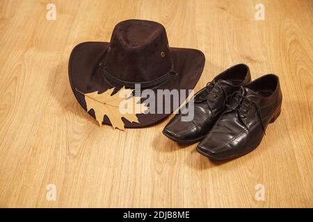 Set von Herren Filzhut mit einem gelben Ahornblatt Und schwarze Schuhe auf einem Holzboden Stockfoto