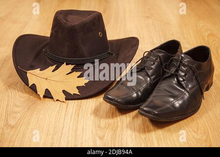 Set von Herren Filzhut mit einem gelben Ahornblatt Und schwarze Schuhe auf einem Holzboden Stockfoto