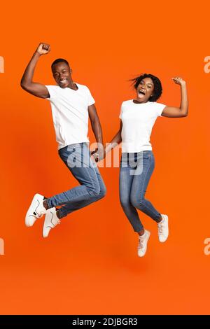Emotionales schwarzes Paar, das die Hände hält und hochspringt Stockfoto