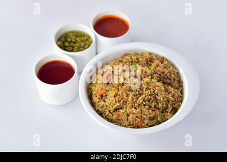 Gebratener Reis in einer Schüssel mit Saucen auf weißem Hintergrund. schezwan gebratener Reis auf weißem Hintergrund mit roten Saucen und Paprika. Stockfoto