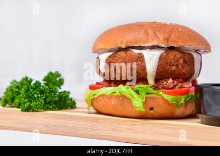 Saftiger Burger mit großem Patty und darauf tropfender Mayonnaise. Fleisch und Gemüse in einem Burger Augenhöhe Foto auf weißem Hintergrund. Stockfoto