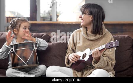 Mutter spielt mit ihrer Tochter zu Hause. Unterricht auf einem Musikinstrument. Entwicklung von Kindern und Familienwerte. Das Konzept der Kinderfreundschaft A Stockfoto