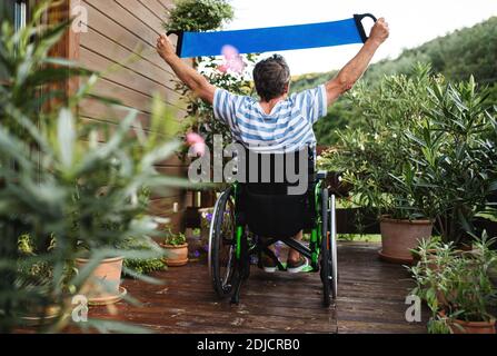 Rückansicht eines älteren Mannes im Rollstuhl, der auf der Terrasse trainieren kann. Stockfoto