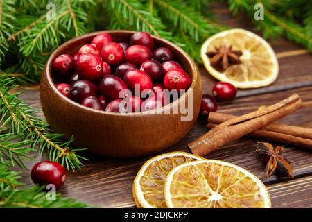 Preiselbeeren frische Beeren in Holzschüssel auf Tisch mit Tanne Äste und getrocknete Orangenscheiben und Zimtstangen Stockfoto