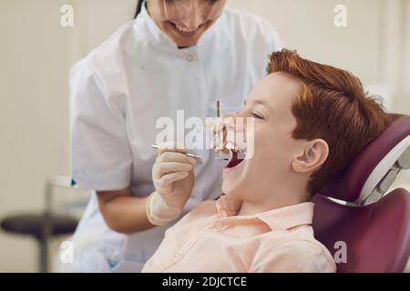 Zahnärztin untersucht die Zähne eines kleinen lächelnden Jungen mit Hilfe spezieller Werkzeuge. Stockfoto