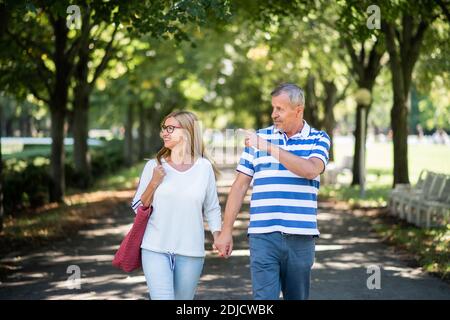 Porträt eines glücklichen älteren Ehepaares, das im Freien in der Stadt oder im Stadtpark spazieren geht. Stockfoto