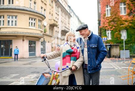 Glückliches Seniorenpaar mit Fahrrad, das auf der Straße in der Stadt spazieren ging und Einkaufstaschen trug. Stockfoto