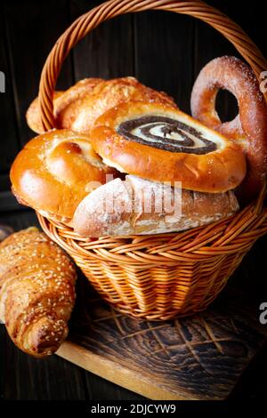 Komposition mit Brot und Brötchen im Korbkorb auf dunklem Hintergrund, vertikales Bild Stockfoto