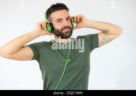 Junger bärtiger Mann mit Kopfhörern auf dem Kopf, der Musik im Stehen hört Isoliert auf weißem Hintergrund mit Kopierbereich Stockfoto