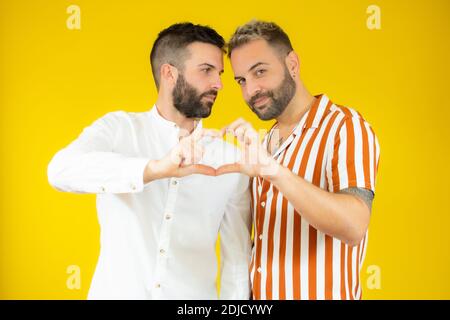 Glücklich Gay paar gekleidet Freizeitkleidung, so dass Herz Form von Fingern, Studio-Porträt auf gelbem Hintergrund Stockfoto
