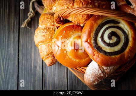 Draufsicht des Sortiments verschiedener Getreidebäcker: Brot, Gebäck, Brötchen, Brezel und Croissant im Korb auf altem Holztisch Stockfoto