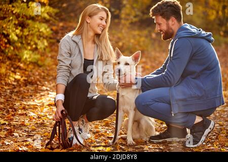 Paar mit Hund zu Fuß. Positive kaukasischen Paar verbringen Zeit mit Hund im Wald, auf dem Land. An sonnigen Herbsttag Stockfoto