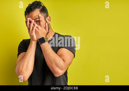Ängstlicher Mann hat Angst vor etwas, Kerl schloss Gesicht mit Händen, Blick auf die Kamera durch die Finger Stockfoto