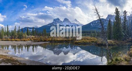 Schneedecke die drei Schwestern Trio Gipfel Berg mit blauem Himmel und weißen Wolken reflektieren auf Wasseroberfläche im Herbst. Schöne Landschaft in Canmore Stockfoto