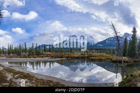 Schneedecke die drei Schwestern Trio Gipfel Berg mit blauem Himmel und weißen Wolken reflektieren auf Wasseroberfläche im Herbst. Schöne Landschaft in Canmore Stockfoto