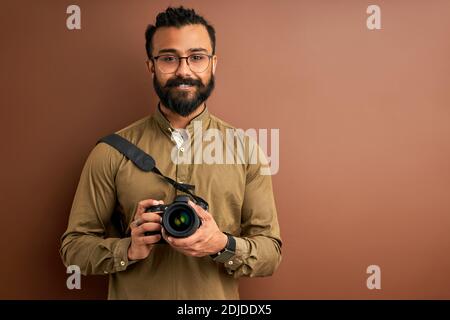 arabischer Mann, der Foto auf Kamera, hält professionelle Kamera in den Händen, trägt Hemd. Posiert. Kreativität und Fotografie Konzept Stockfoto