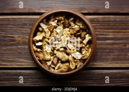 Walnüsse in runder Schale auf Holztisch. Geschälte trockene Walnusskerne auf braunem Hintergrund, gesunde Ernährung, Draufsicht Stockfoto