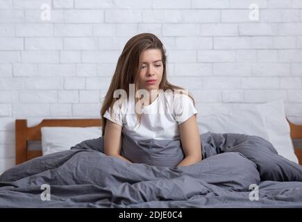 Junge Frau, die allein in ihrem Bett sitzt, in den Weltraum starrt und an einer klinischen Depression leidet Stockfoto