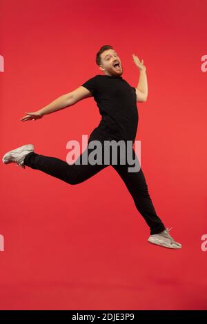 Inspiriert. In voller Länge Porträt von jungen erfolgreichen High-Springen Mann Gestik isoliert auf rotem Studio-Hintergrund. Attraktive männliche kaukasische Modell. Copyspace. Menschliche Emotionen, Gesichtsausdruck Konzept. Stockfoto