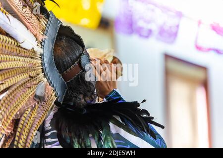 Selektiver Fokus der Rückansicht des Menschen in traditioneller Kleidung, mit Hut verziert mit Feder Blasmuschel in Altar während Dia de los muertos in Mexiko Stockfoto