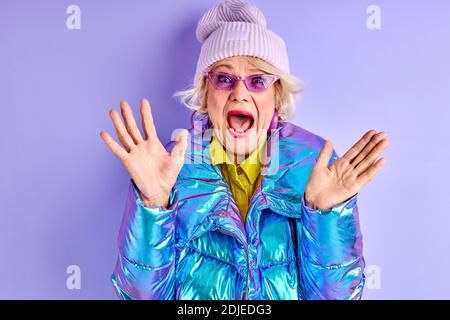 Ältere Frau schreit, feiert den Sieg oder Geburtstag, stehen mit geöffnetem Mund und ausgebreiteten Armen, isoliert Stockfoto