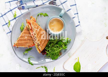 Gegrillte Club Sandwich Panini mit Rindfleisch, Tomaten, Käse, Salat und einer Tasse Kaffee. Leckeres Frühstück oder Snack. Draufsicht, Overhead, Flat Lay Stockfoto