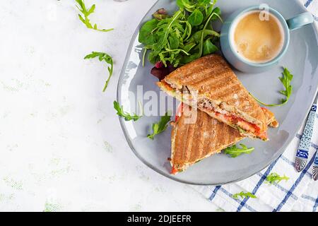 Gegrillte Club Sandwich Panini mit Rindfleisch, Tomaten, Käse, Salat und einer Tasse Kaffee. Leckeres Frühstück oder Snack. Draufsicht, Overhead, Flat Lay Stockfoto