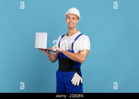 Mann in Overalls und Hardhut mit Laptop-Computer auf Blauer Hintergrund Stockfoto