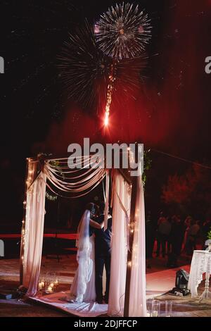 Glücklich umarmt Braut und Bräutigam beobachten schöne bunte Feuerwerk in den Nachthimmel. Hochzeitstag, Party. Stockfoto