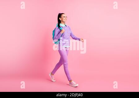 In voller Länge Profil Foto von schönen Dame zu Fuß tragen Spezifikationen Rucksack lila Pullover Hose Sneakers isoliert rosa Farbe Hintergrund Stockfoto